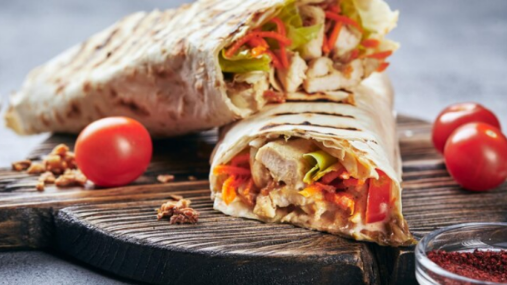 A picture of paratha roll with some tomatoes and red chilly powders placed.