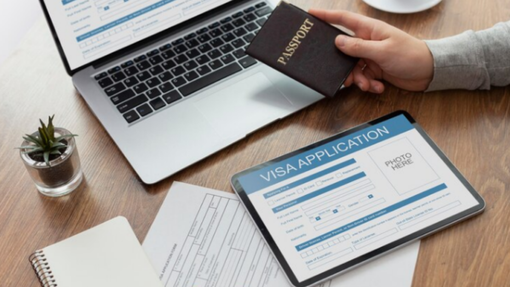 An image of a laptop, Ipad and some papers on table with a person holding a passport.