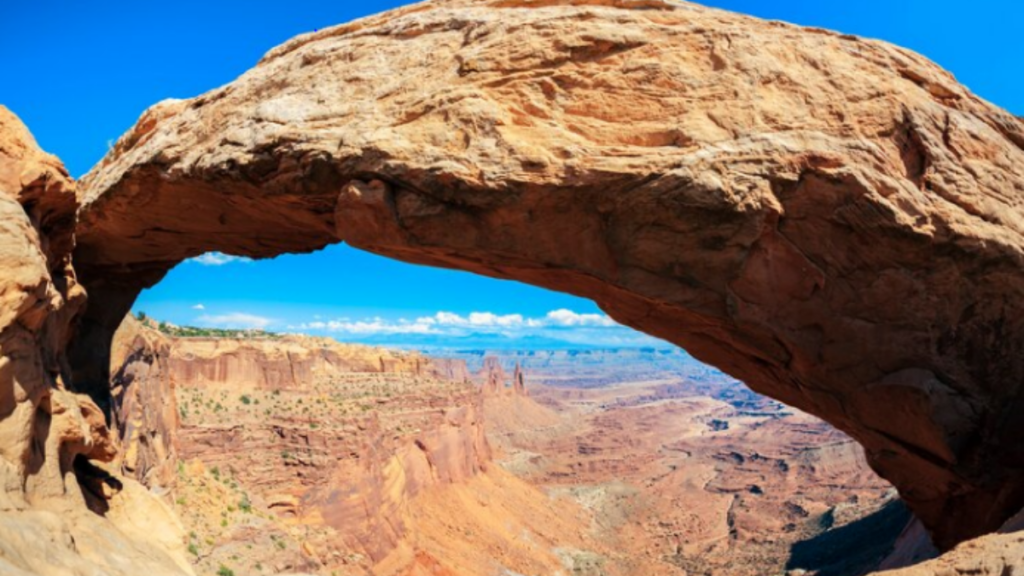 An image of Arches National Park with a sandy rock with mountains at the background.