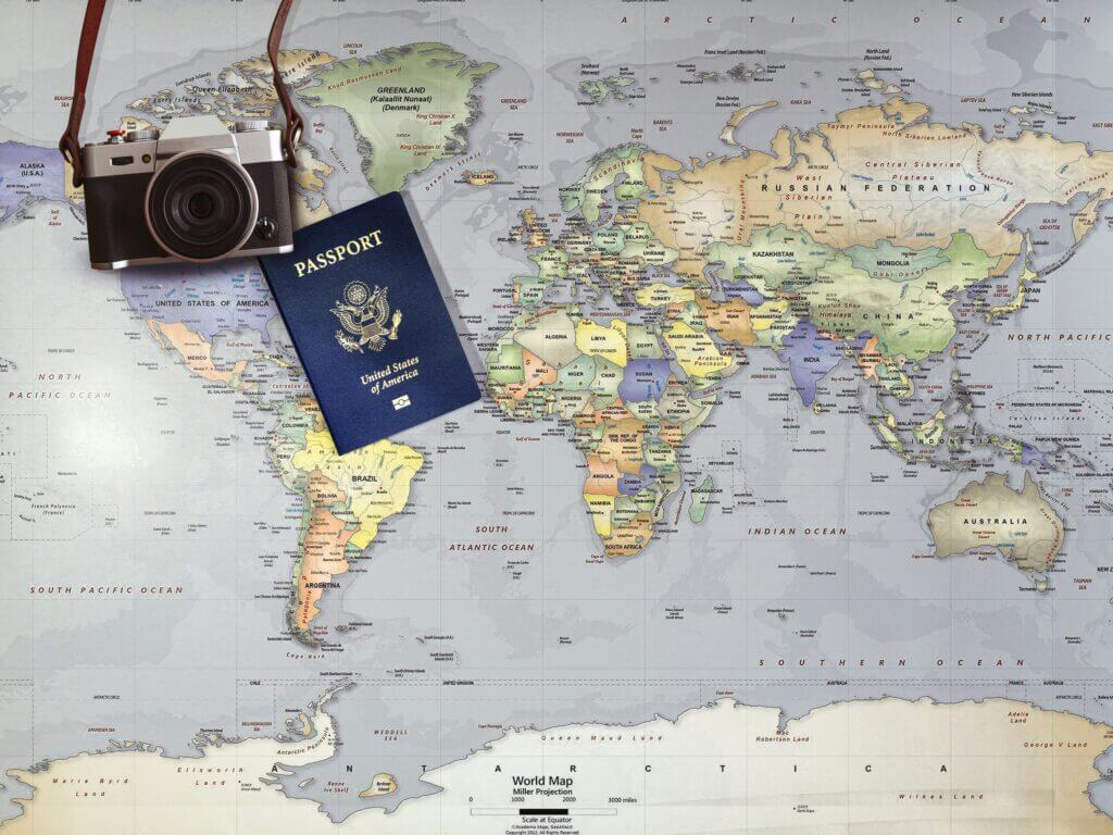 A picture of a world map with a us passport and old age digital camera placed on it.